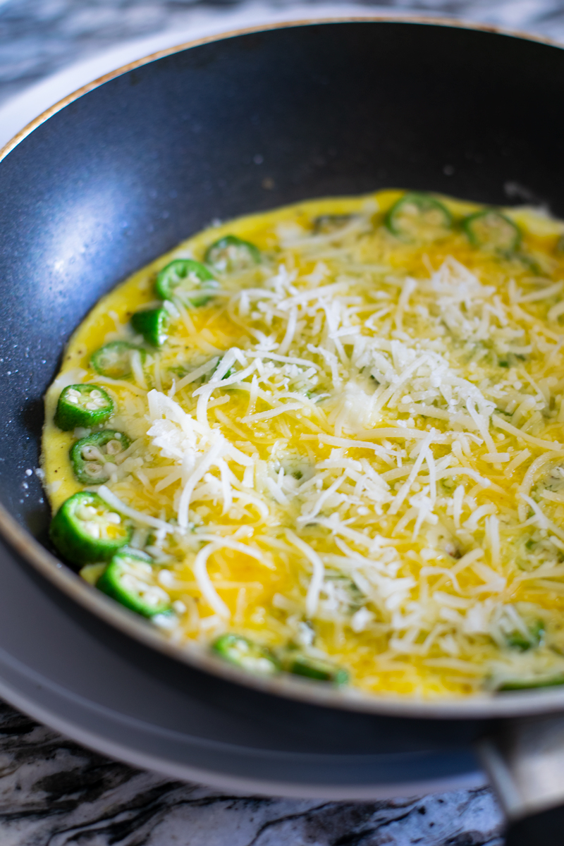 egg and okra cooking in frypan with shredded cheese on top