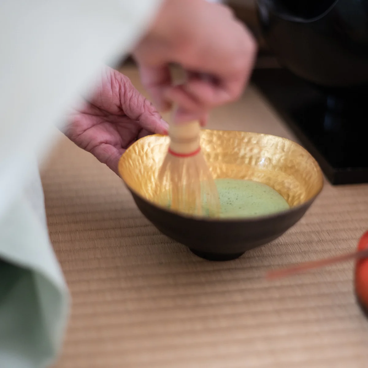 whisking matcha with bamboo chasen in golden chawan tea bowl