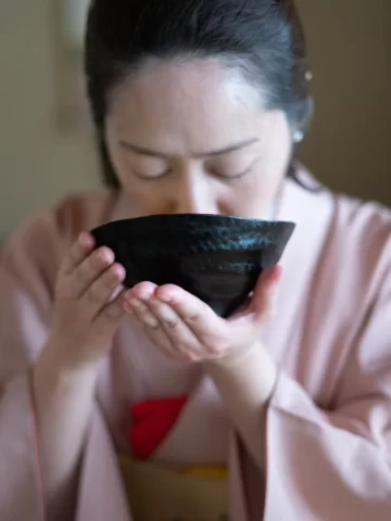 Japanese woman in kimono drinking tea from black chawan
