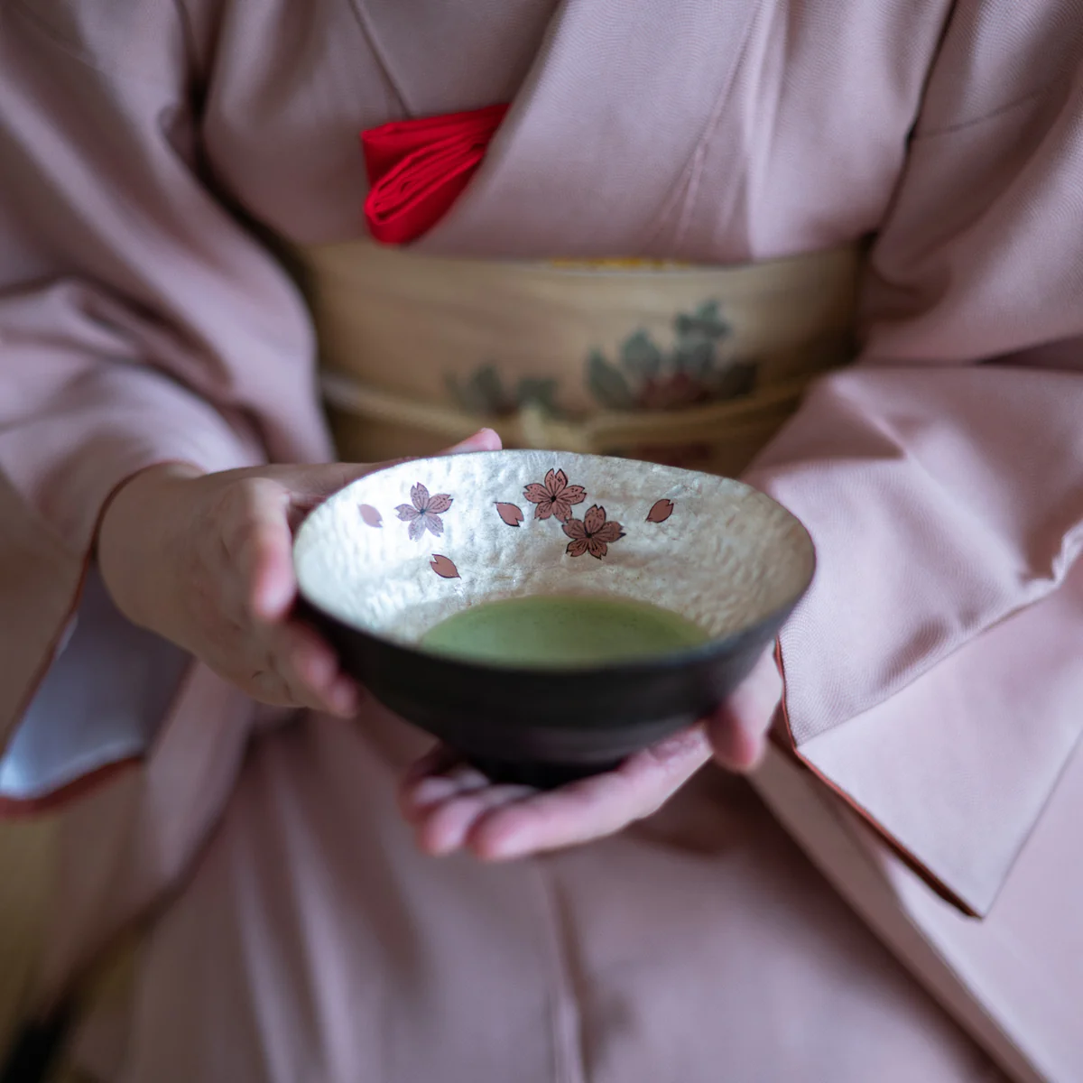 Japanese woman in kimono holding matcha chawan with gold and sakura decor