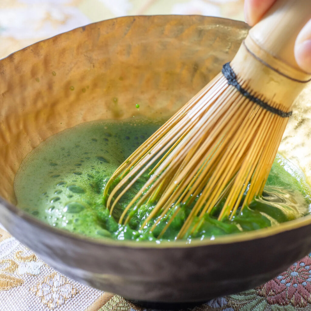 matcha being whisked in a chawan tea bowl with a bamboo whisk