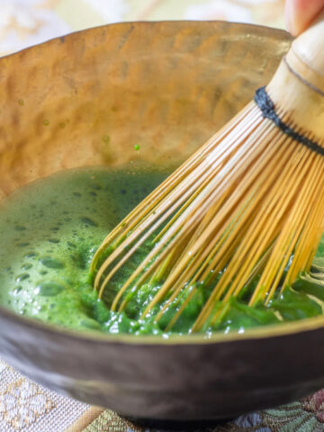 whisking matcha with water in a chawan tea bowl with bamboo whisk