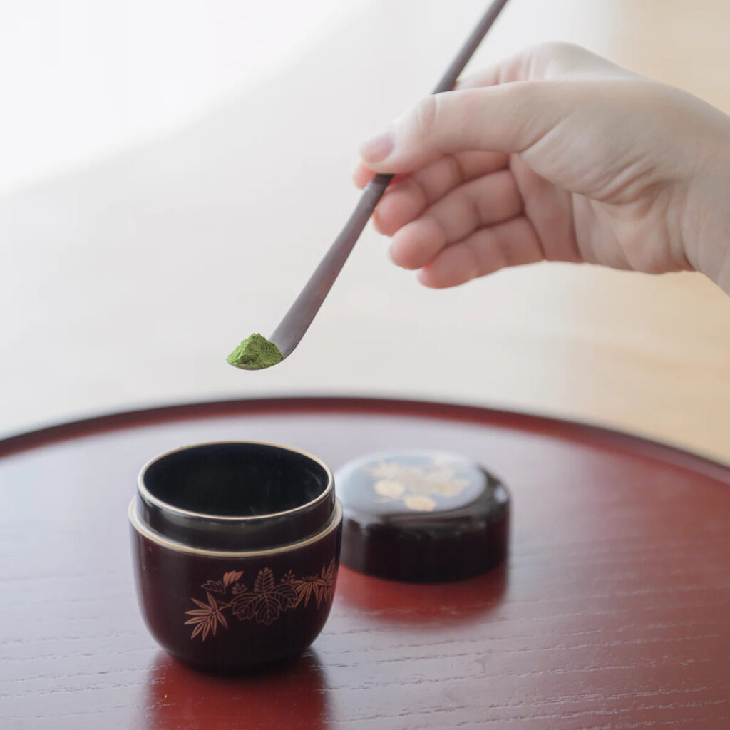a hand scooping matcha with a Japanese traditional. bamboo scoop