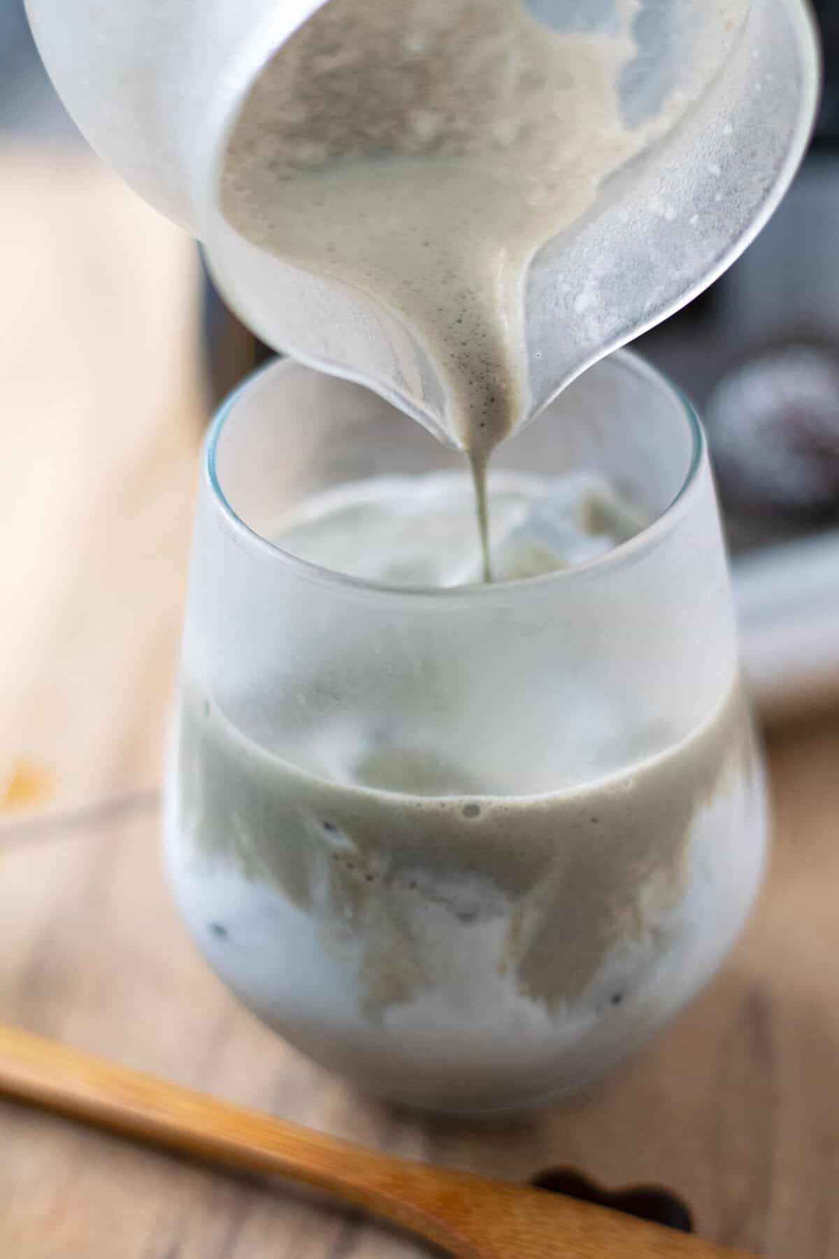 Pouring black sesame latte into frosted glass filled with ice and milk with grey and white swirls.