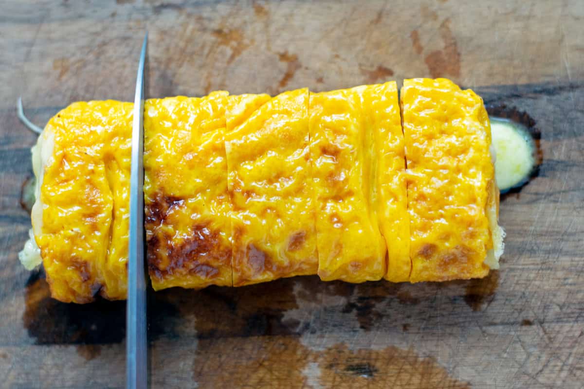 Slicing a Japanese rolled omelet into 5 slices with a sharp knife. Warm mozzarella cheese is oozing out one end. 