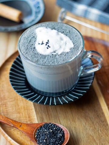 Black sesame latte in glass mug, sprinkled with a few black sesame seeds.