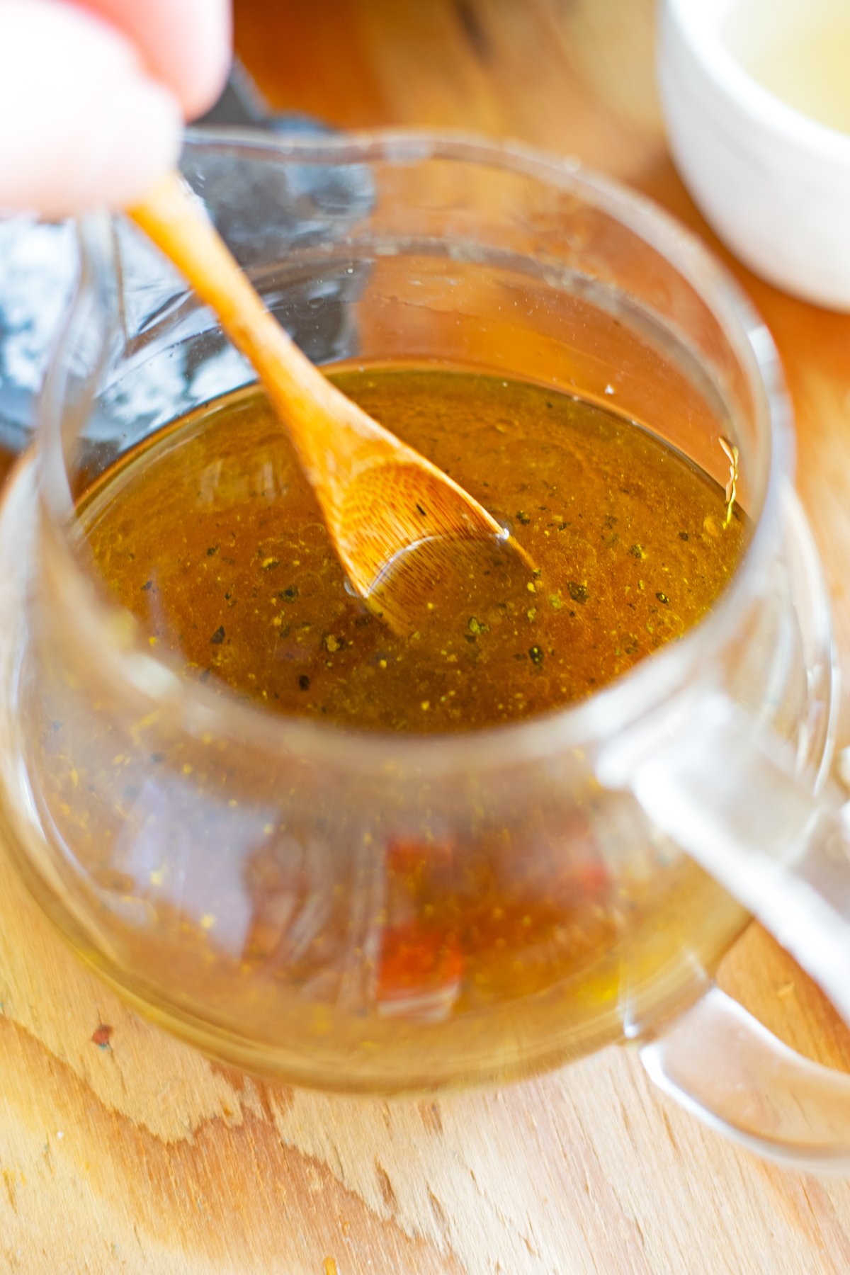 Wooden spoon mixing salt and pepper into salad dressing.