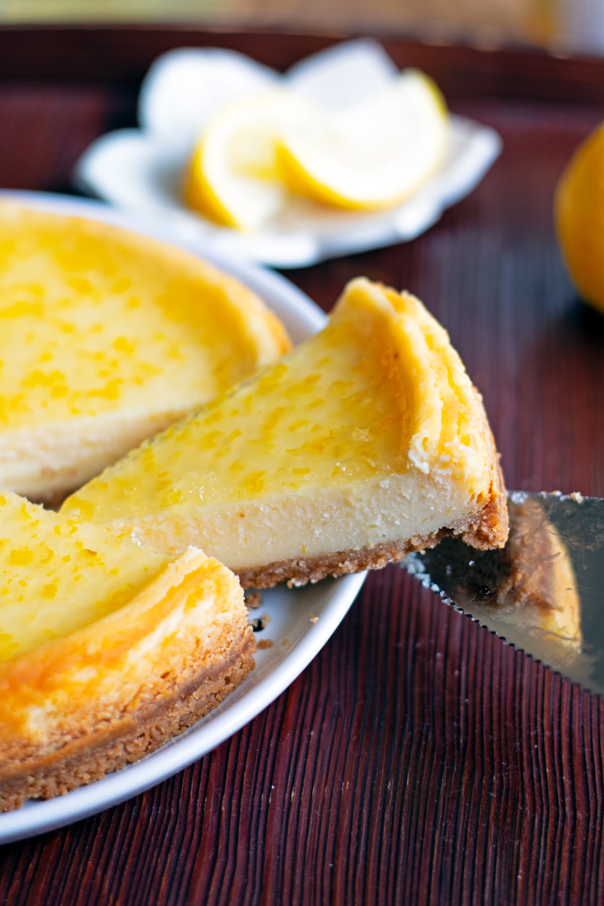 Lifting up a piece of yuzu-jelly covered yuzu cheesecake with a silver cake server. 