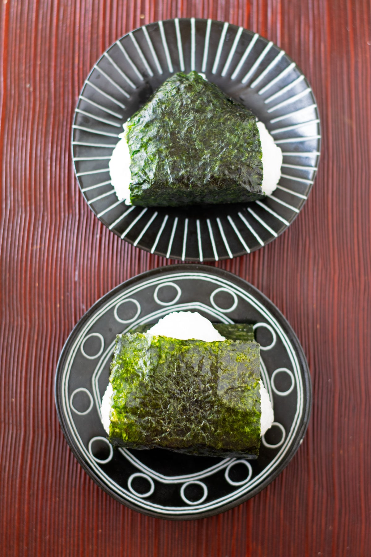 Onigiri wrapped with nori in two different ways on plates.