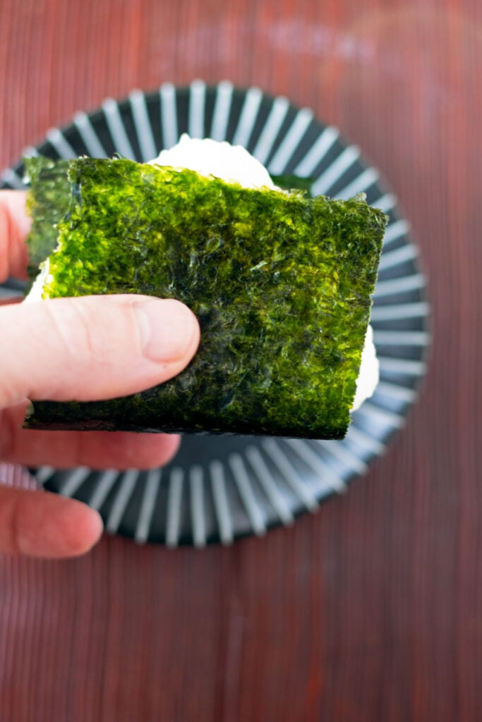 A hand holding one onigiri that was just wrapped with a crisp sheet of nori seaweed.