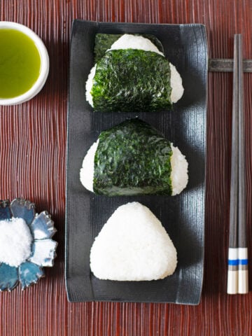 Onigiri wrapped with nori seaweed and one plain shio onigiri with no nori and cup of green tea.