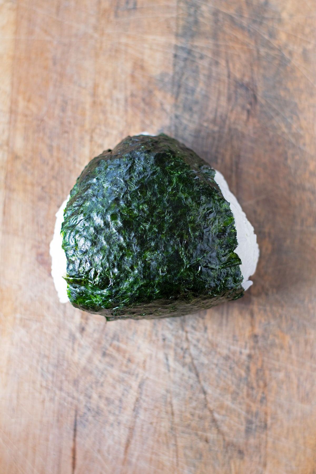 An onigiri wrapped fully with nori on a wooden cutting board.