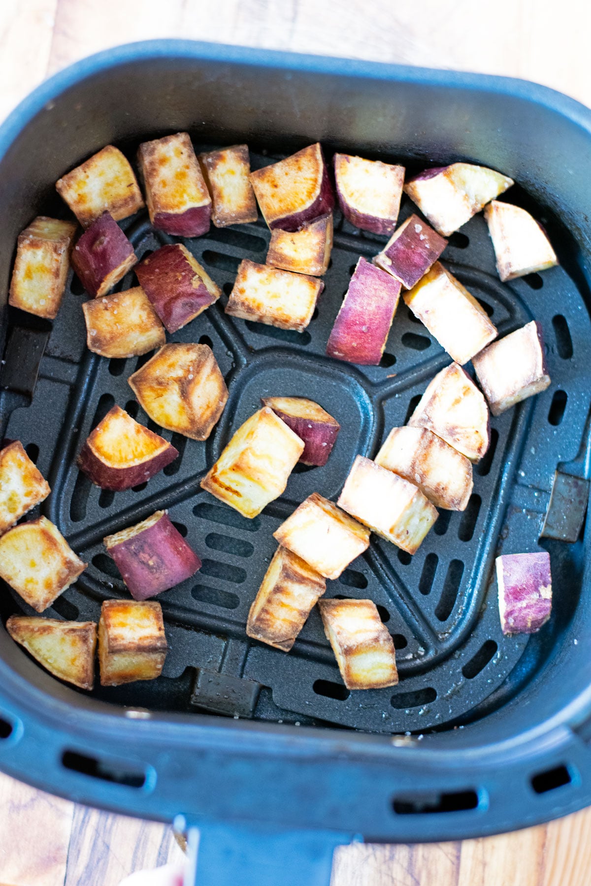 Cooked Japanese sweet potato cubes in air fryer basket with golden edges.