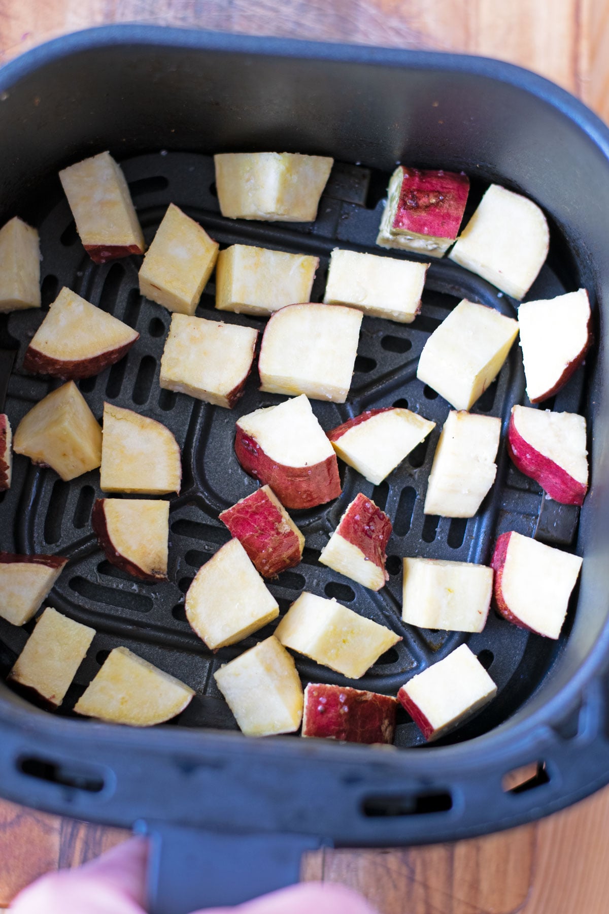 Air fryer basket with sweet potato cubes before cooking.