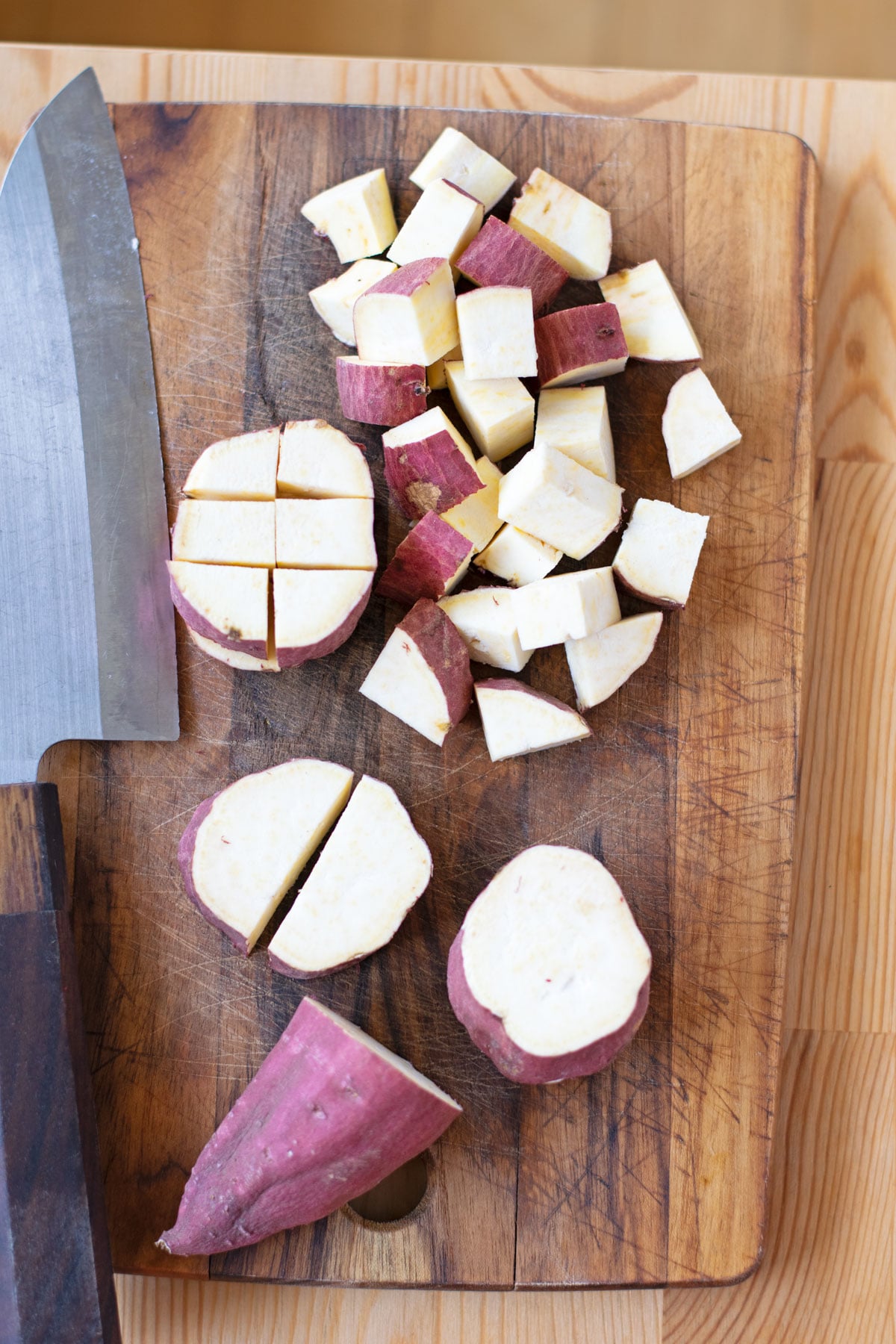 Cut Japanese sweet potato cubes on cutting board with knife.