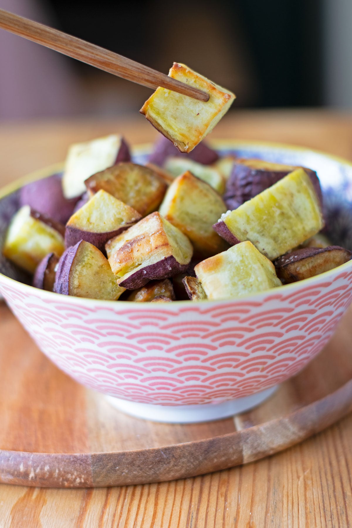 Chopsticks picking up a golden air fryer Japanese sweet potato cube from a bowl.