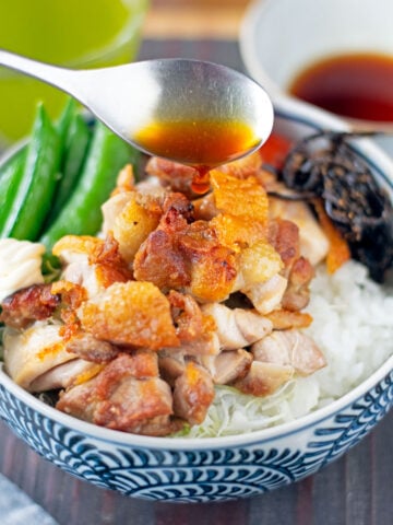 Spoon pouring yuzu sauce over bowl of grilled chicken and vegetables.