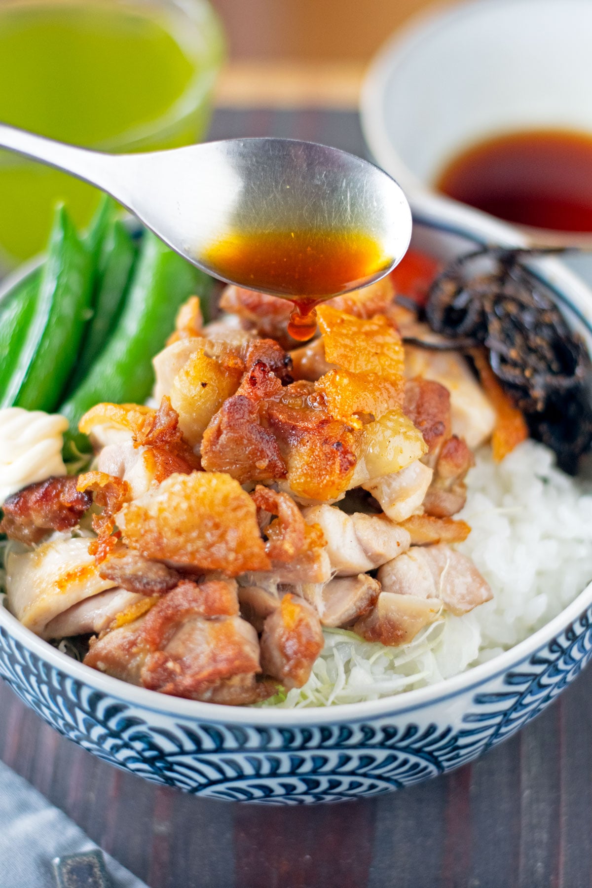 Pouring a spoonful of yuzu sauce over a grilled chicken donburi with veggies.