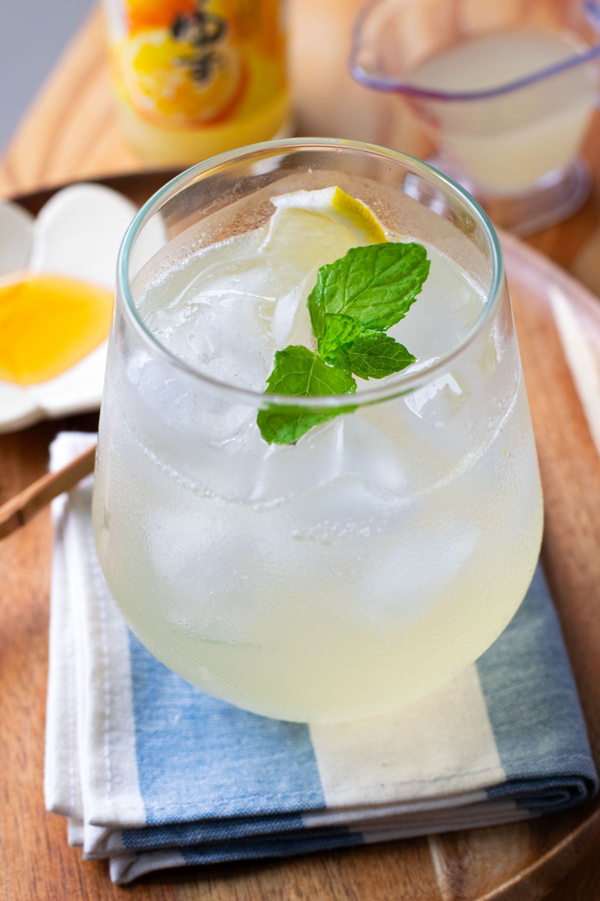 A yuzu mocktail in a glass with ice, garnished with a sprig of mint and a thin slice of lemon.