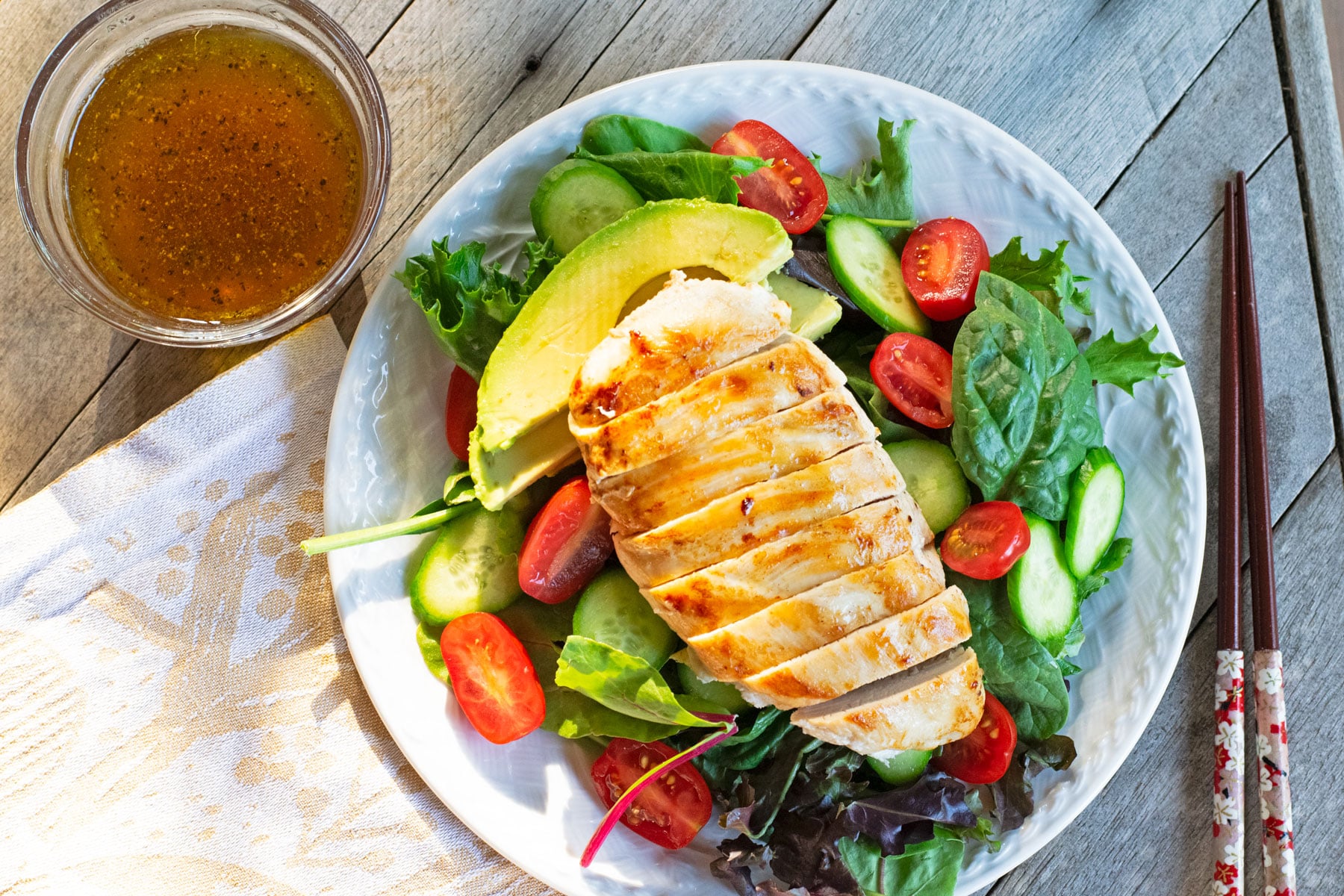 Sautéed chicken with mixed greens, avocado, sliced cucumber, and cherry tomatoes, served with homemade yuzu salad dressing in a small glass bowl on the side.