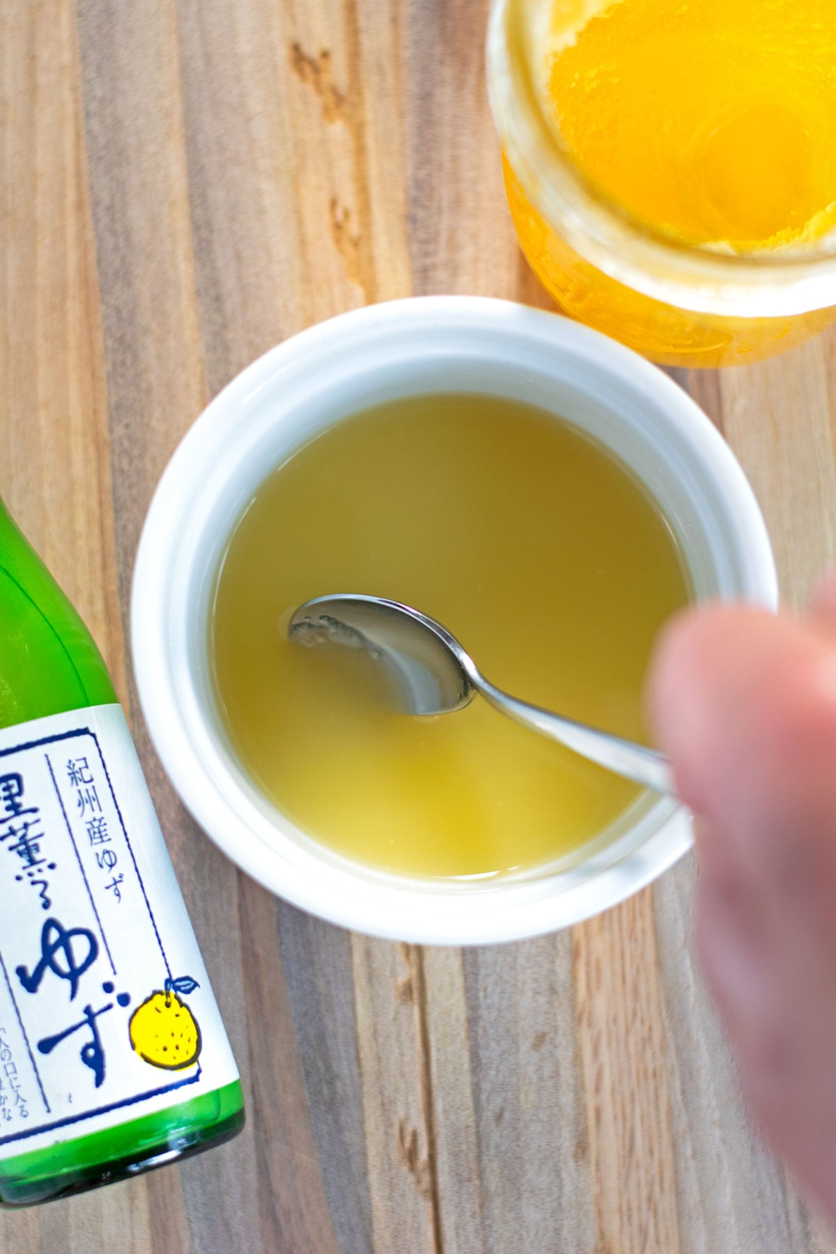 Bottled yuzu juice and honey being stirred together in a small bowl to make a yuzu mocktail.