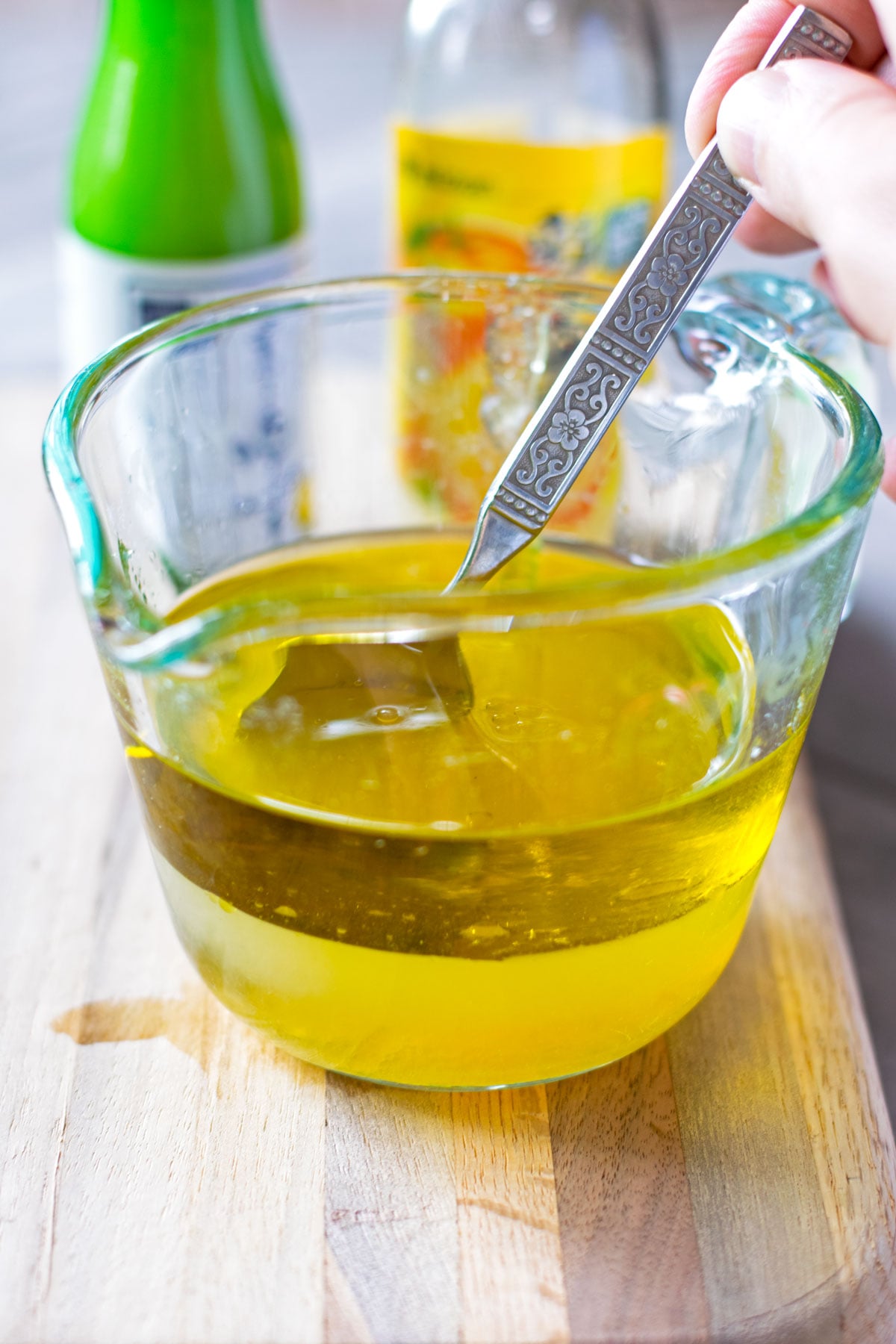 A spoon mixing yuzu salad dressing in a Pyrex glass measuring cup.