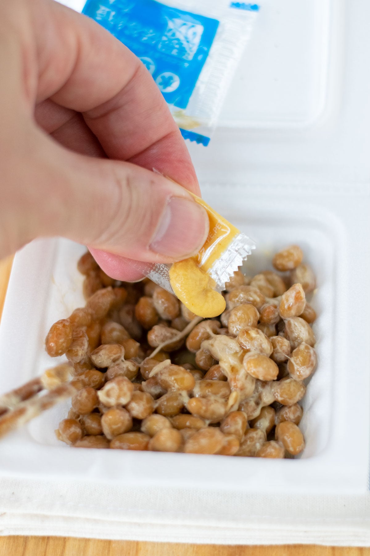 Squeezing the karashi from a small packet on top of natto inside a styrofoam container.