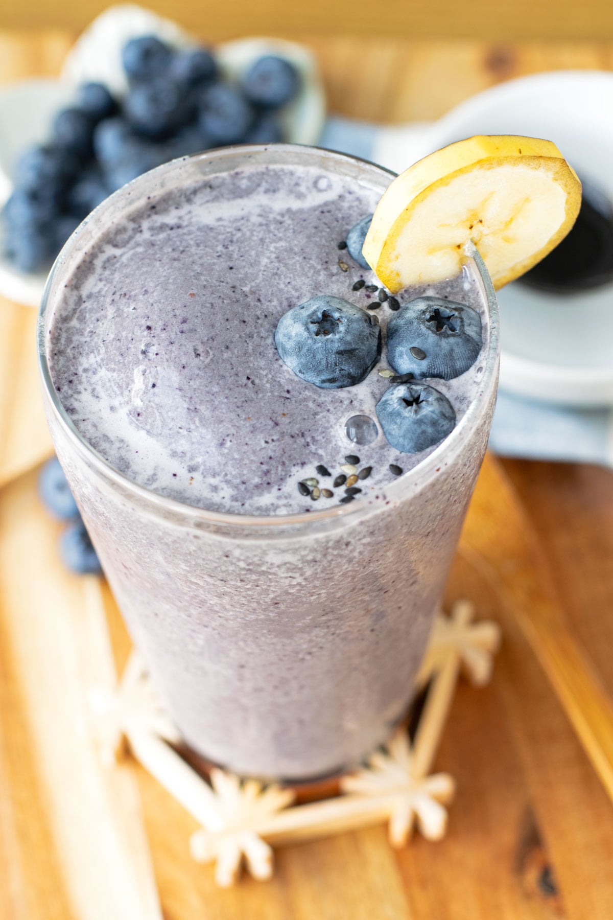 Kurogoma black sesame smoothie with fresh blueberries and black sesame seeds sprinkled on top. A thin slice of banana in its peel attached to the rim of the glass.