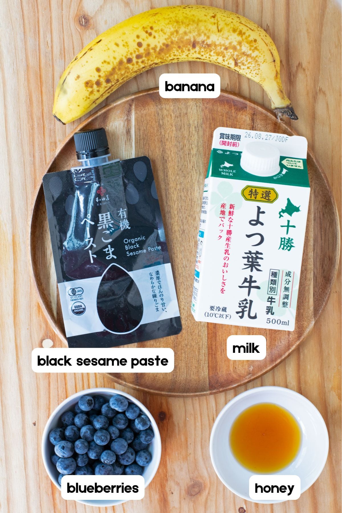 Ingredients for a black sesame smoothie: banana, milk, black sesame paste, honey, and blueberries.