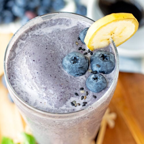 Black sesame smoothie garnished with bleberries, banana slice, and a sprinkle of black sesame seeds