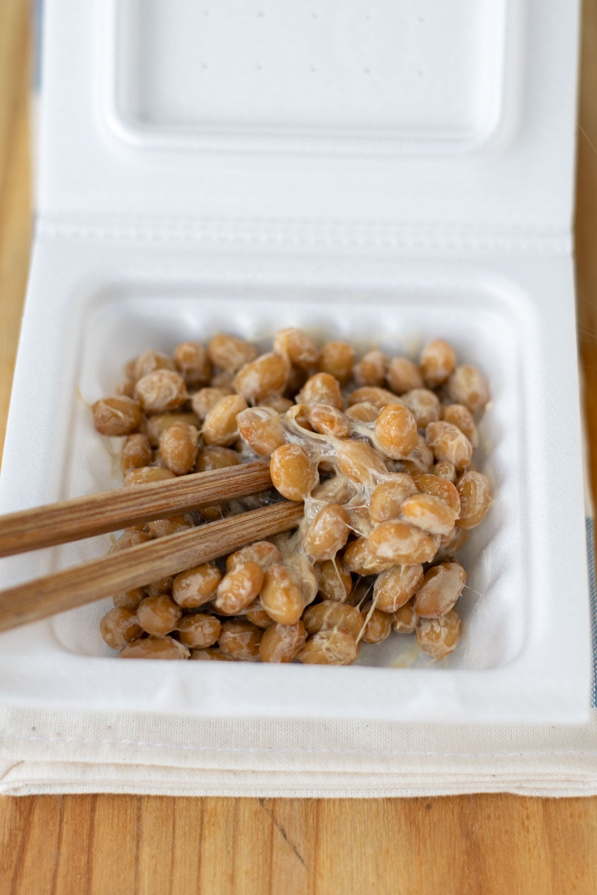 Chopsticks mixing natto inside the styrofoam container.