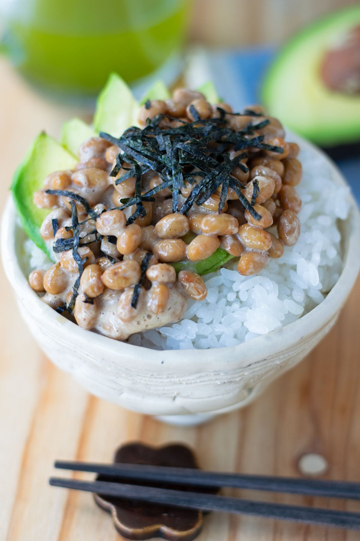 A bowl of white rice topped with thinly sliced avocado, natto, and kizami nori.