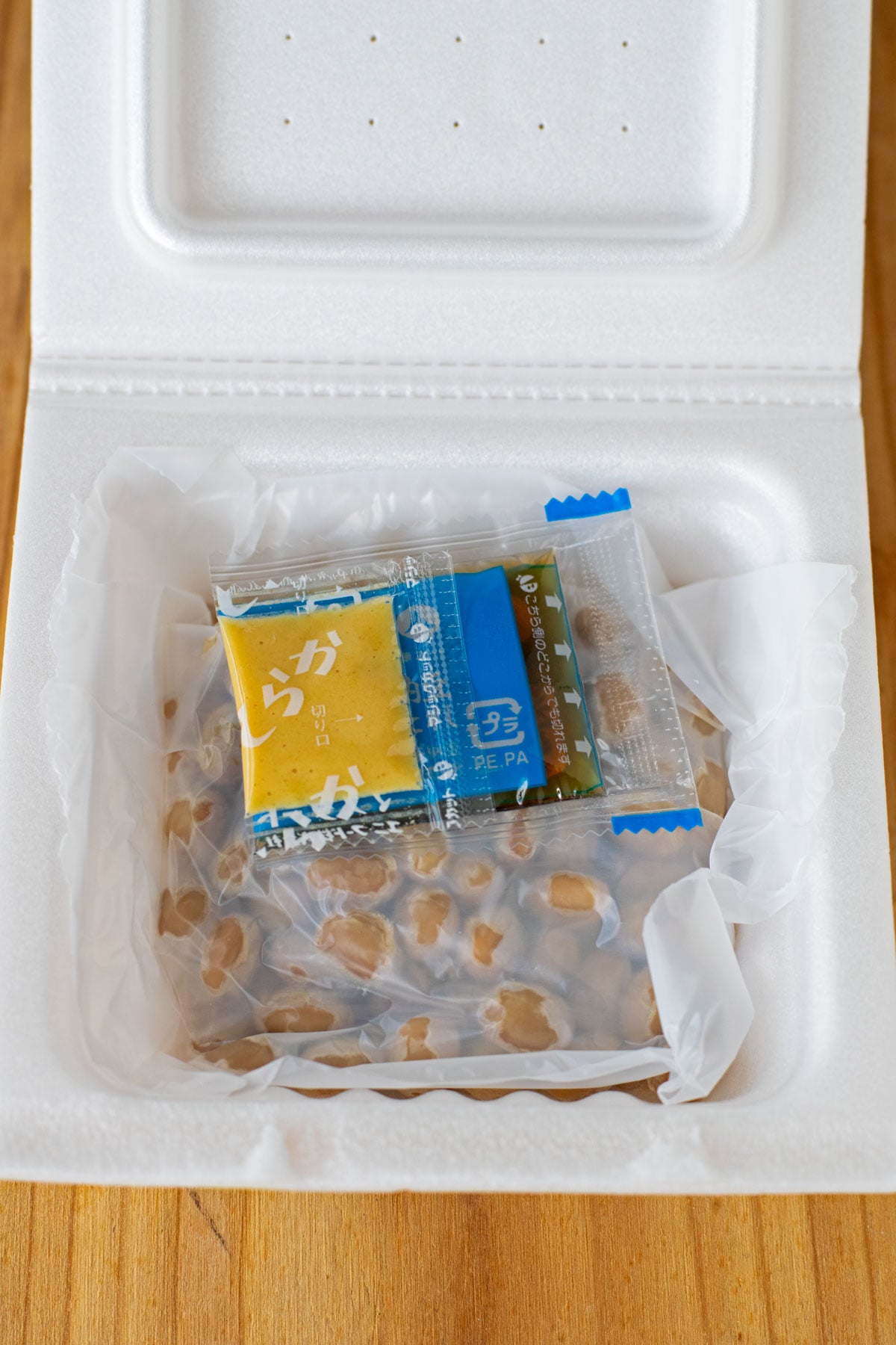A styrofoam package of natto with karashi mustard and a packet of tare sauce.