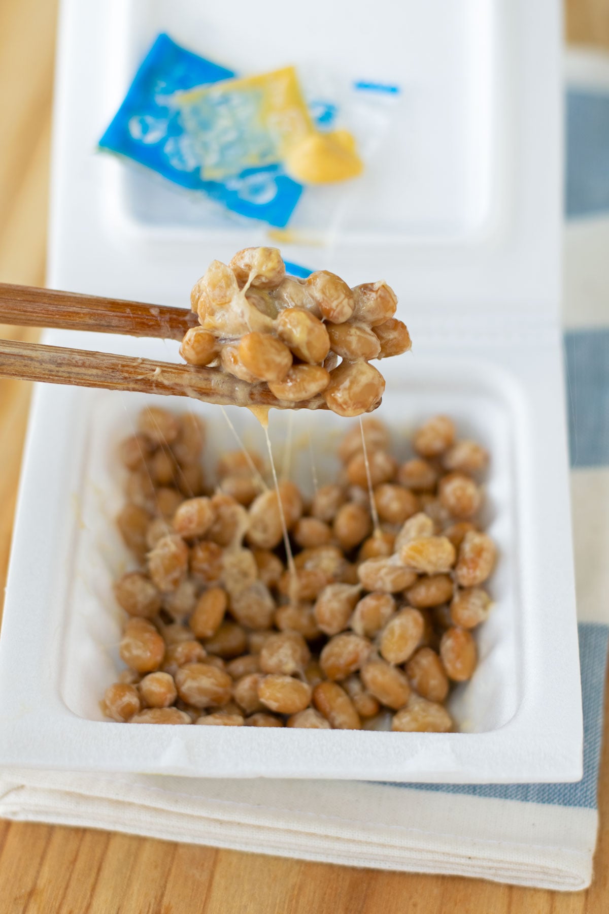Chopsticks picking up a bite-full of natto that's been stirred and mixed with karashi mustard and tare sauce.
