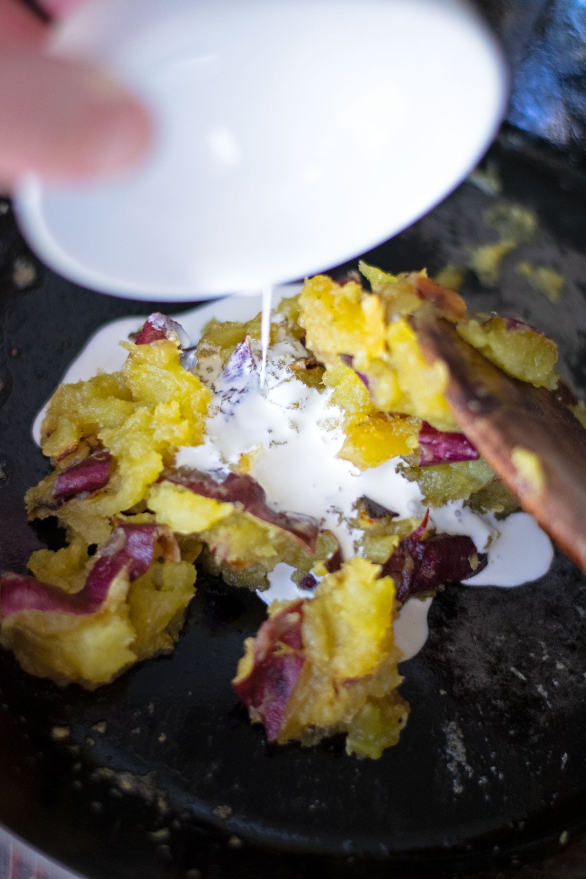 Pouring heavy cream on top of mashed satsumaimo Japanese sweet potatoes.