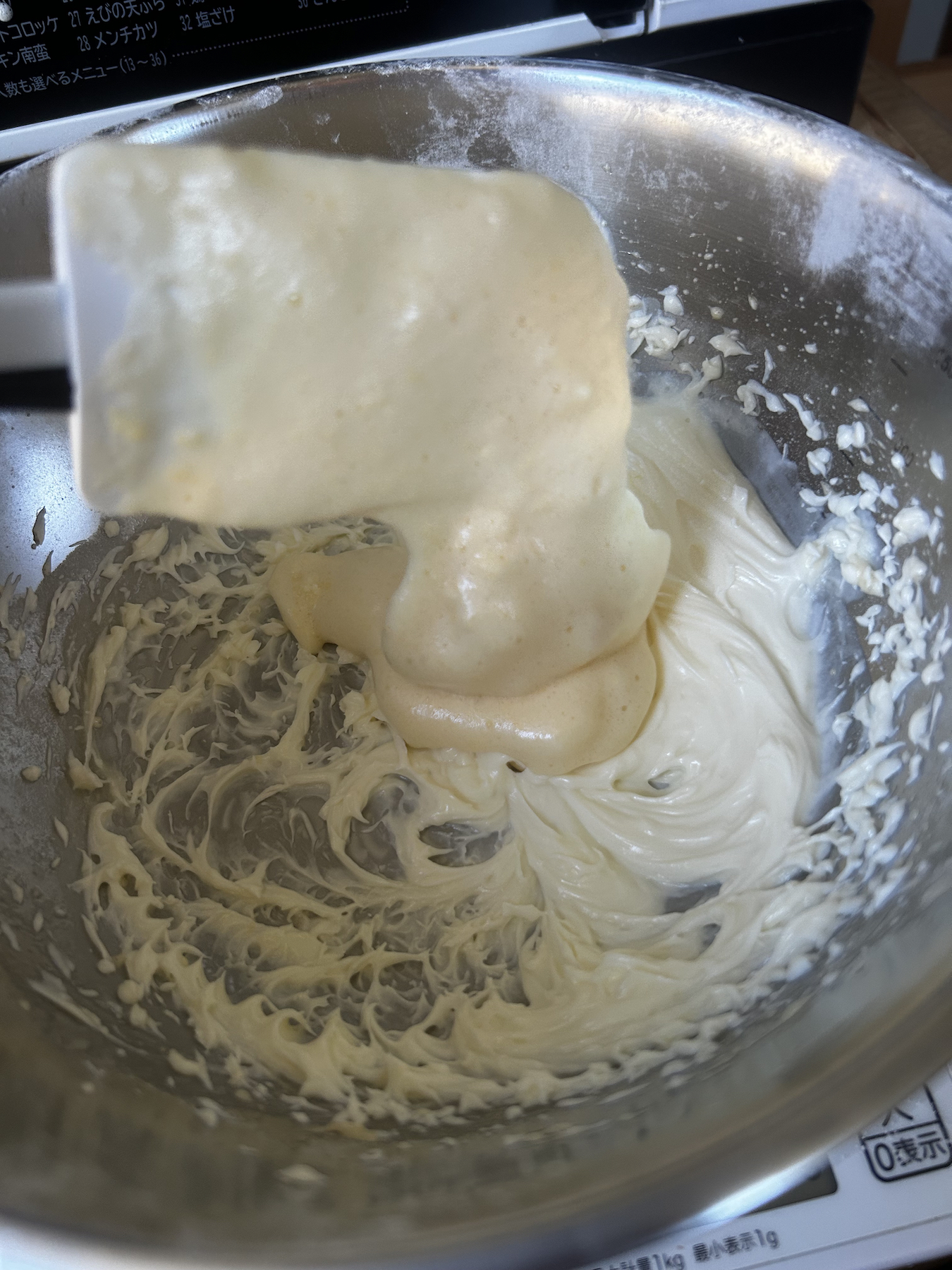 A spatula added a scoop of egg batter to butter batter in a metal bowl.