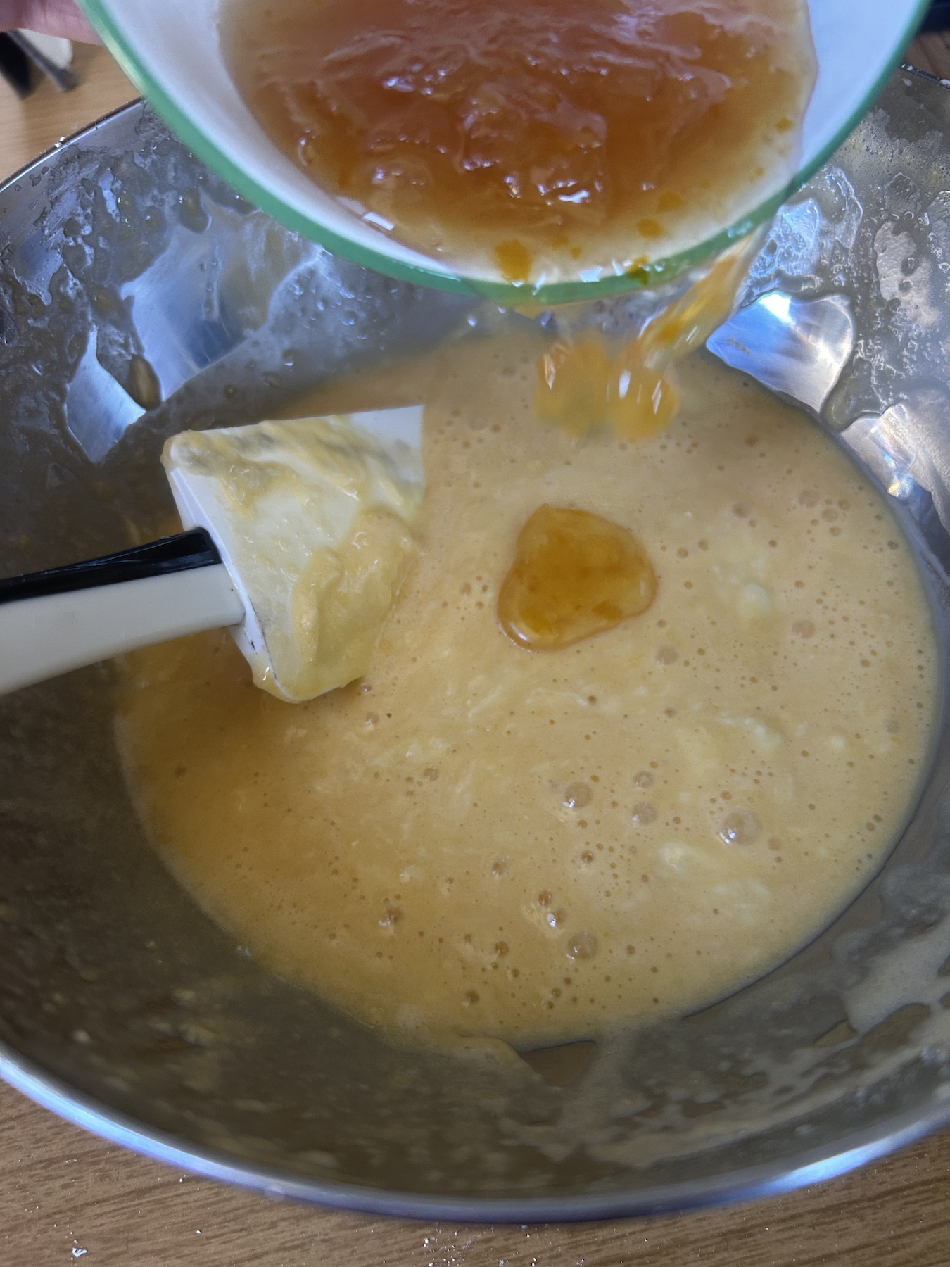 Pouring yuzu cha into cake batter in a metal bowl.