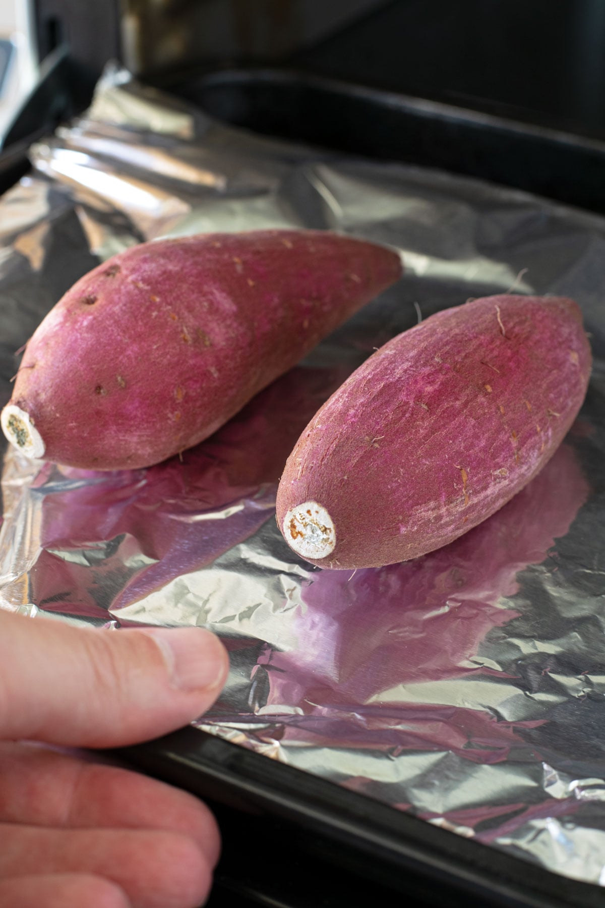 Putting two Japanese sweet potatoes in the oven on a baking pan covered with foil.