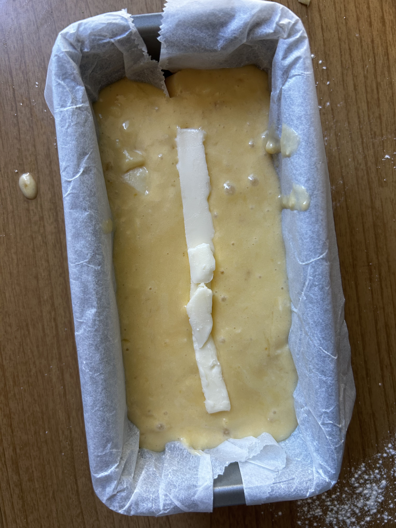 A long strip of butter along the centerline of cake batter inside a cake pan lined with parchment paper.