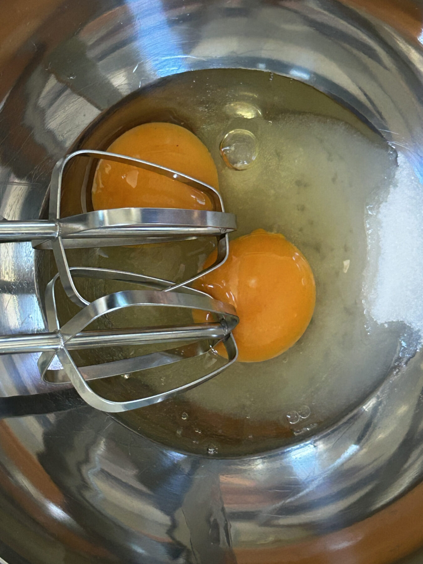 Eggs and sugar in a mixing bowl with hand mixer.