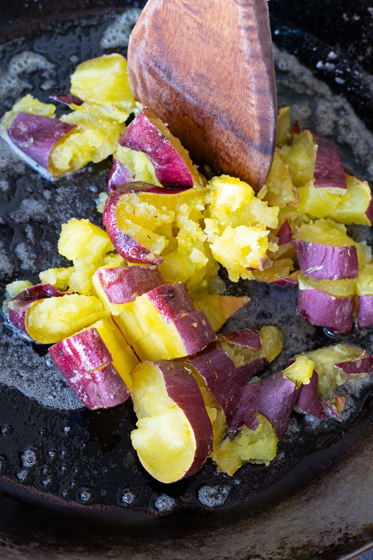 Mashing Japanese sweet potatoes in a fry pan with melted butter.