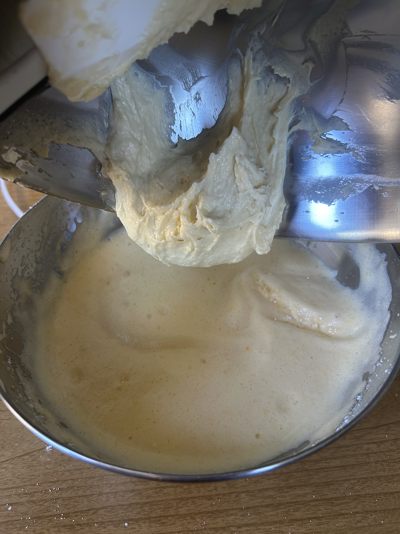 Pouring butter and sour cream batter into egg and sugar batter in a metal bowl.
