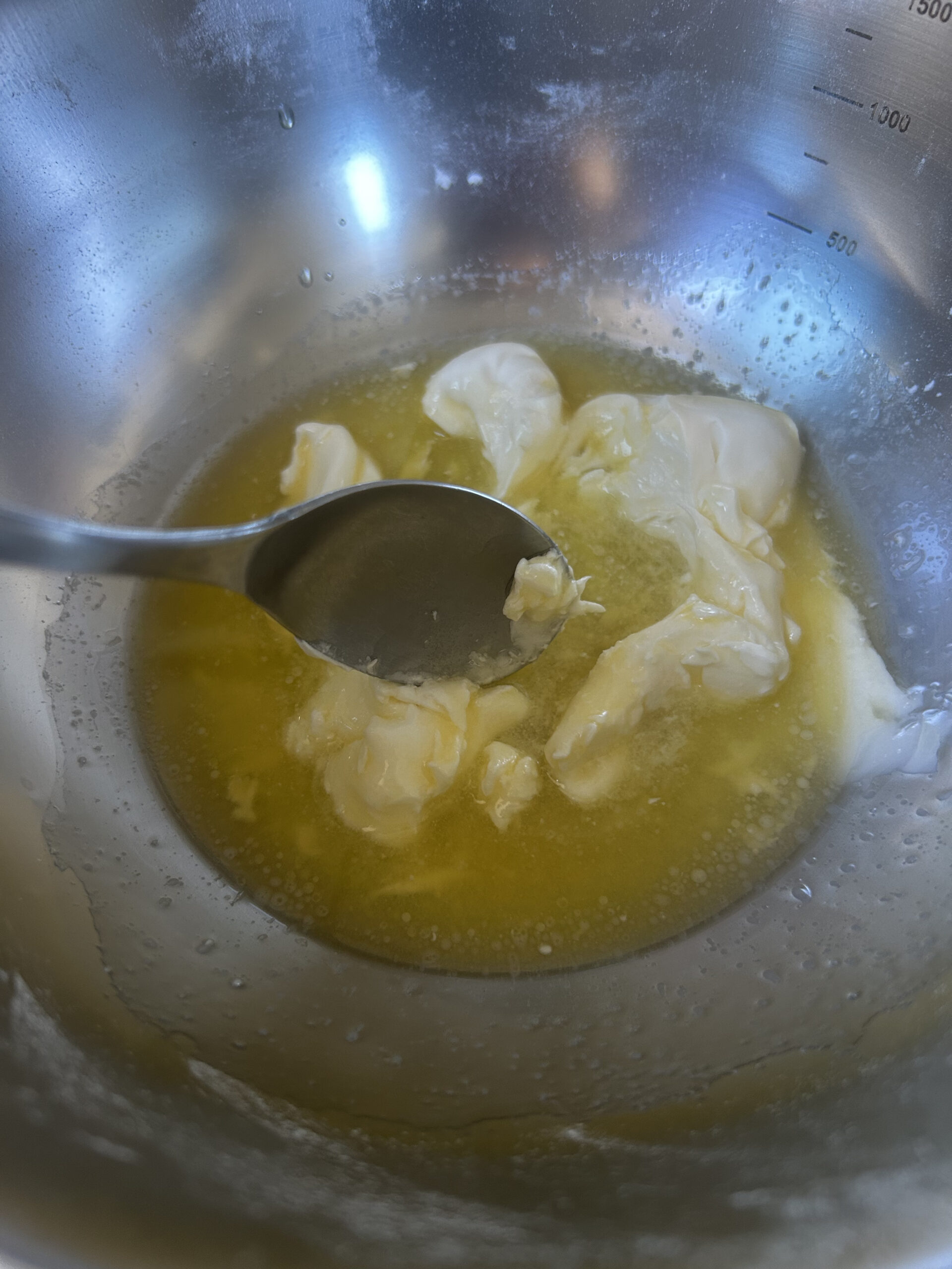 A spoon mixing together melted butter and sour cream in a metal bowl.
