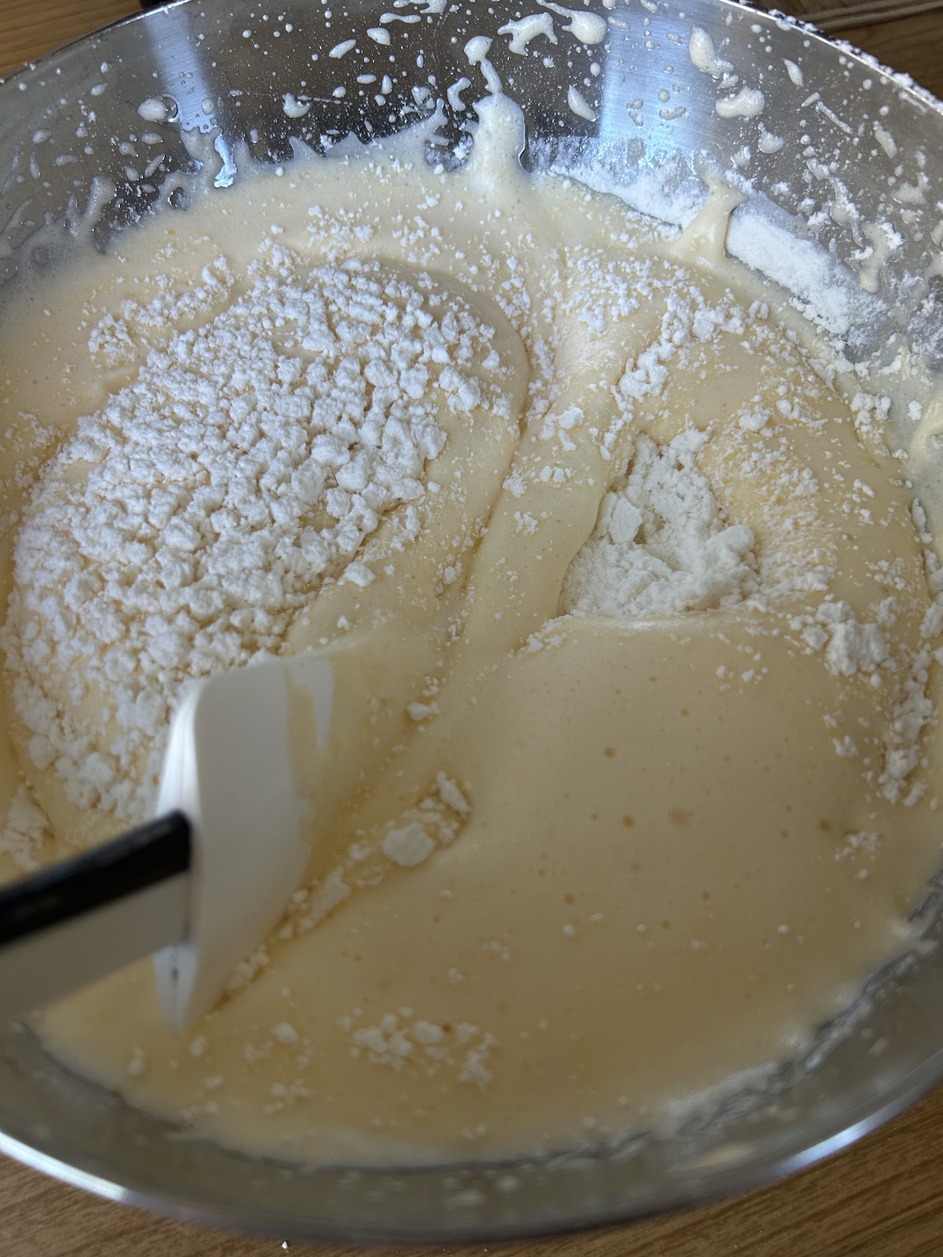 A spatula folding flour with a cutting, scooping motion into a batter.