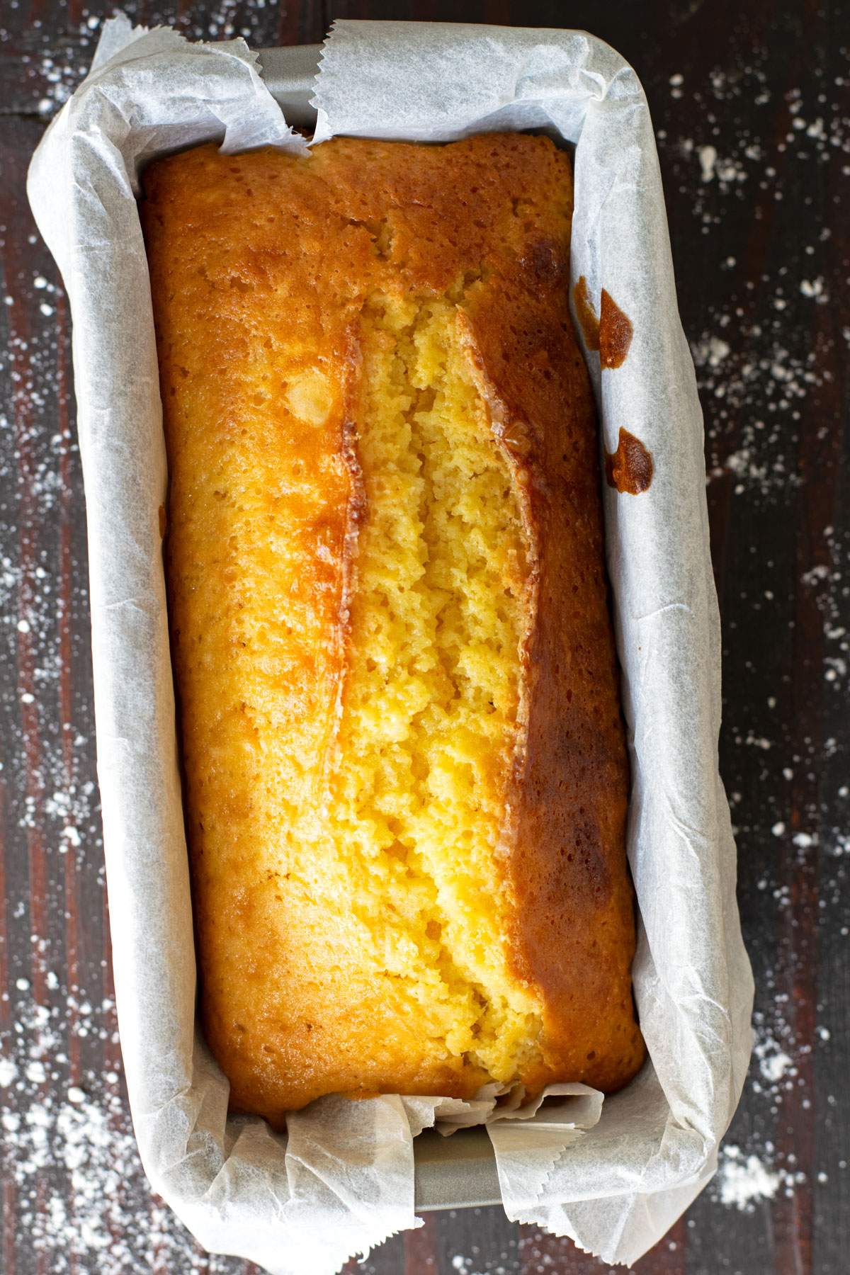 Whole yuzu pound cake in pan with flour sprinkled on the table.