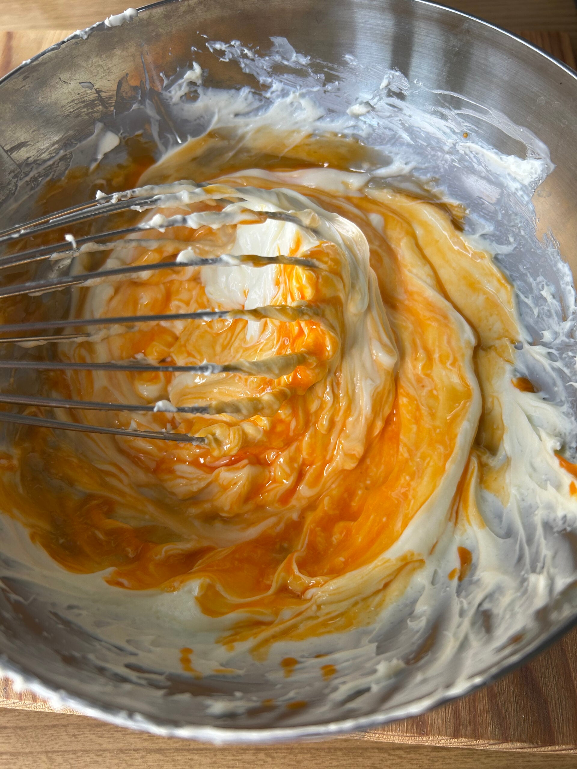 Whisking egg yolks into cheesecake batter in a metal mixing bowl.