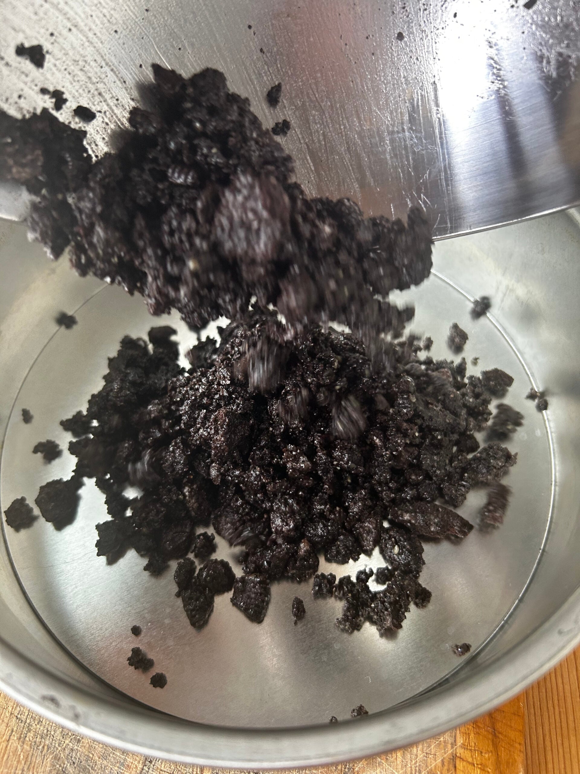 Adding Oreo black sesame powder butter mix to a springform pan.