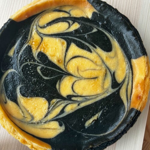 Whole marbled black sesame cheesecake on a cutting board with metal server.