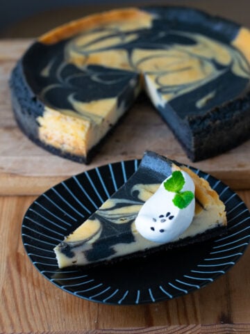 Slice of marbled black sesame cheesecake garnished with whip cream, mint, and and sprinkle of black sesame seeds.