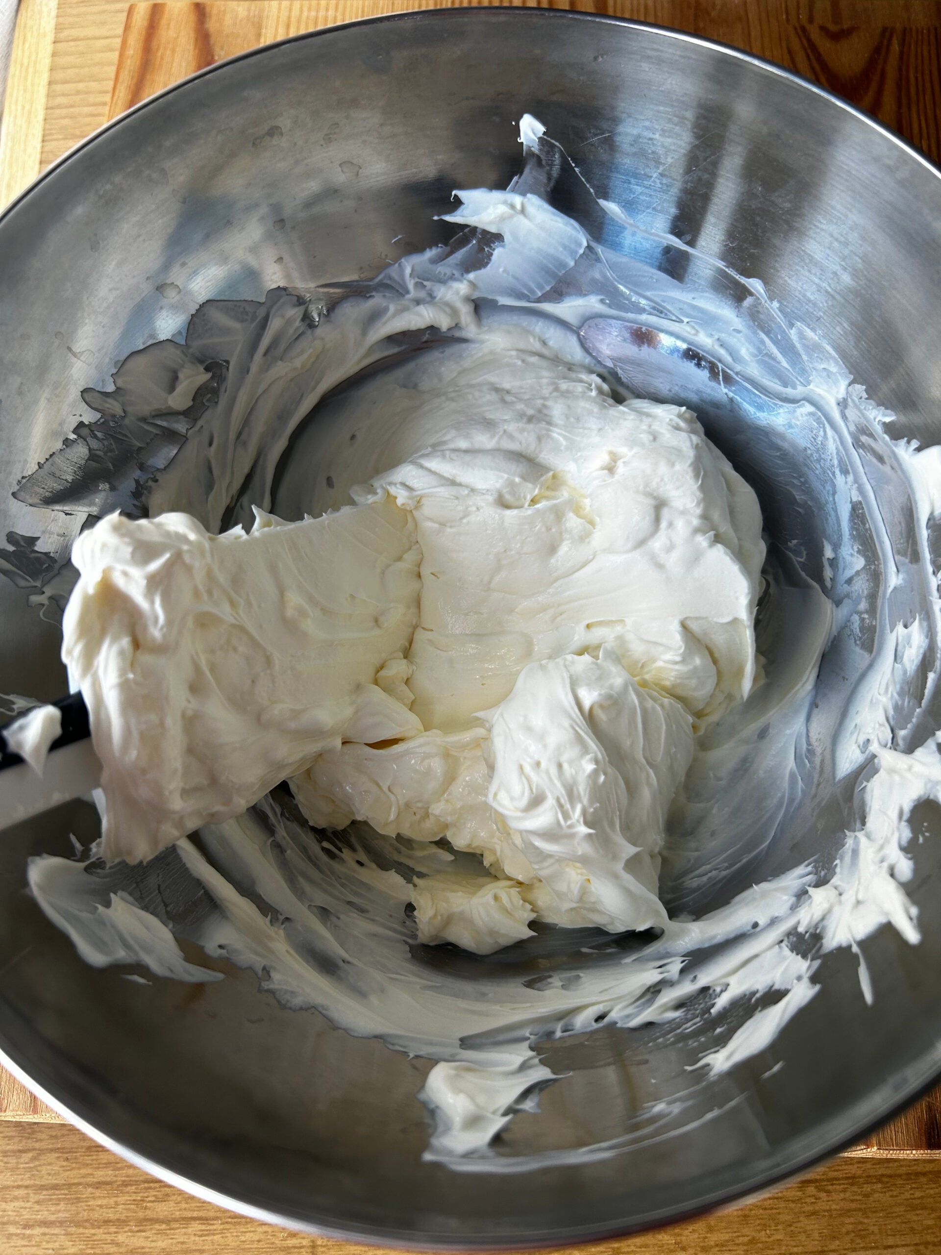 Mixing cream cheese and sour cream inside a metal mixing bowl.